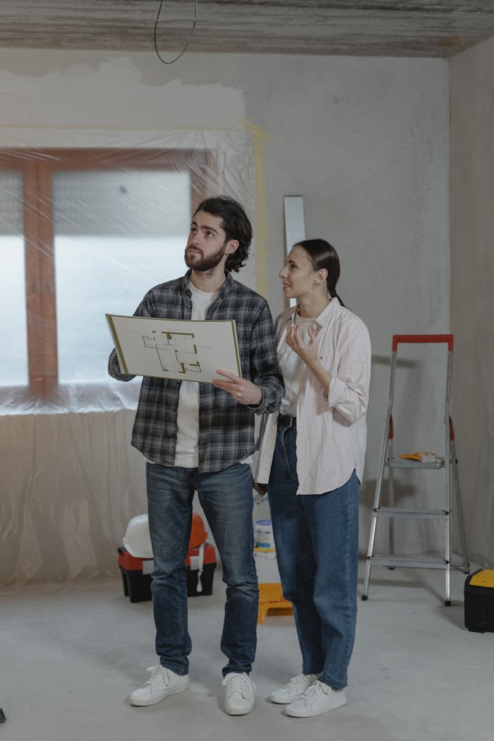 A couple reviews floor plans during a home renovation, surrounded by tools.